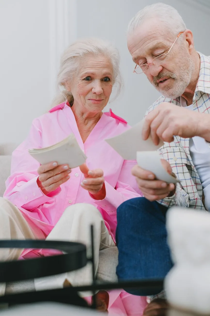 A senior couple sitting indoors, reminiscing over old photographs at home.