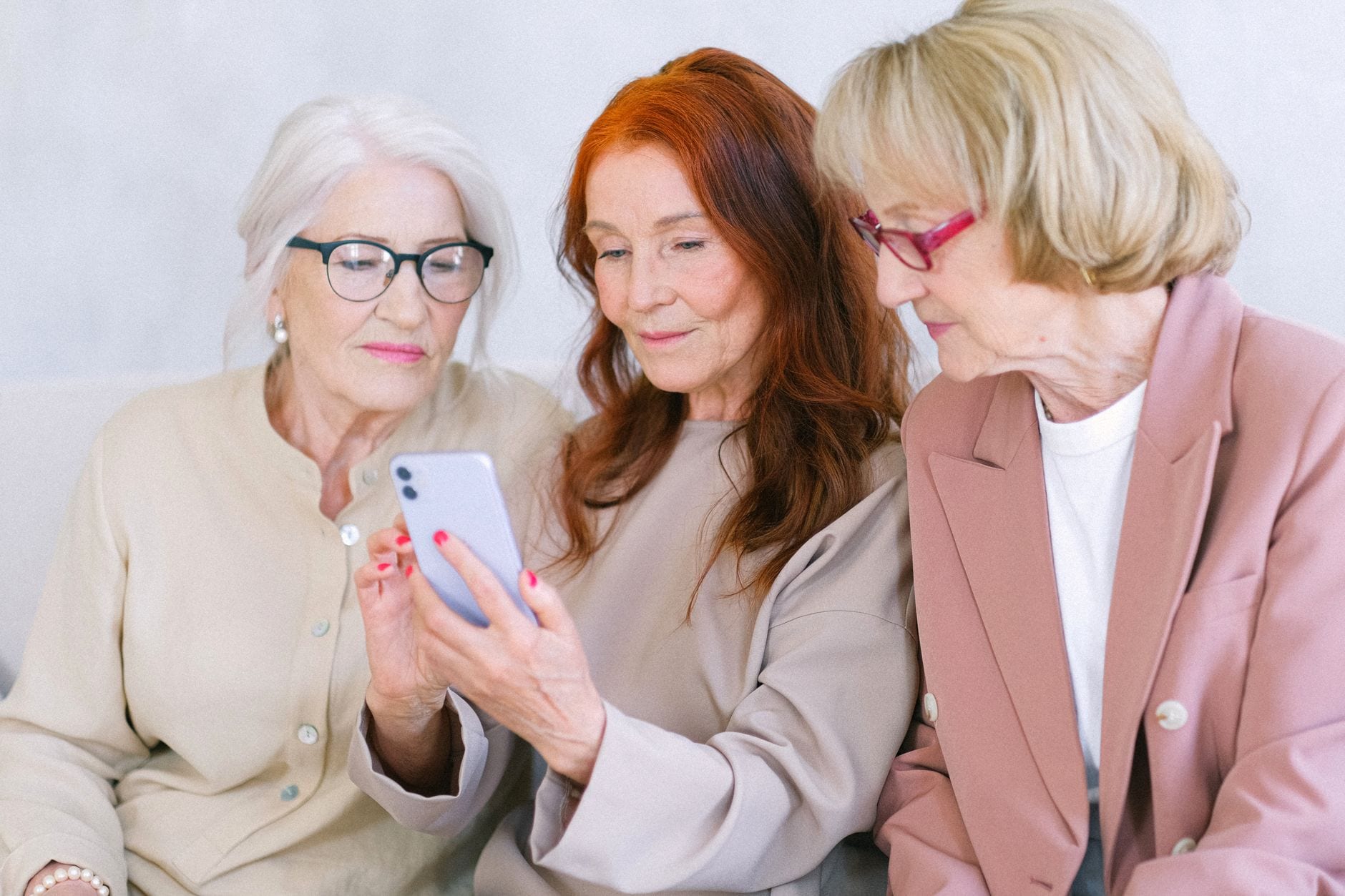 Senior women in elegant outfit using mobile phone while sitting together and looking at screen