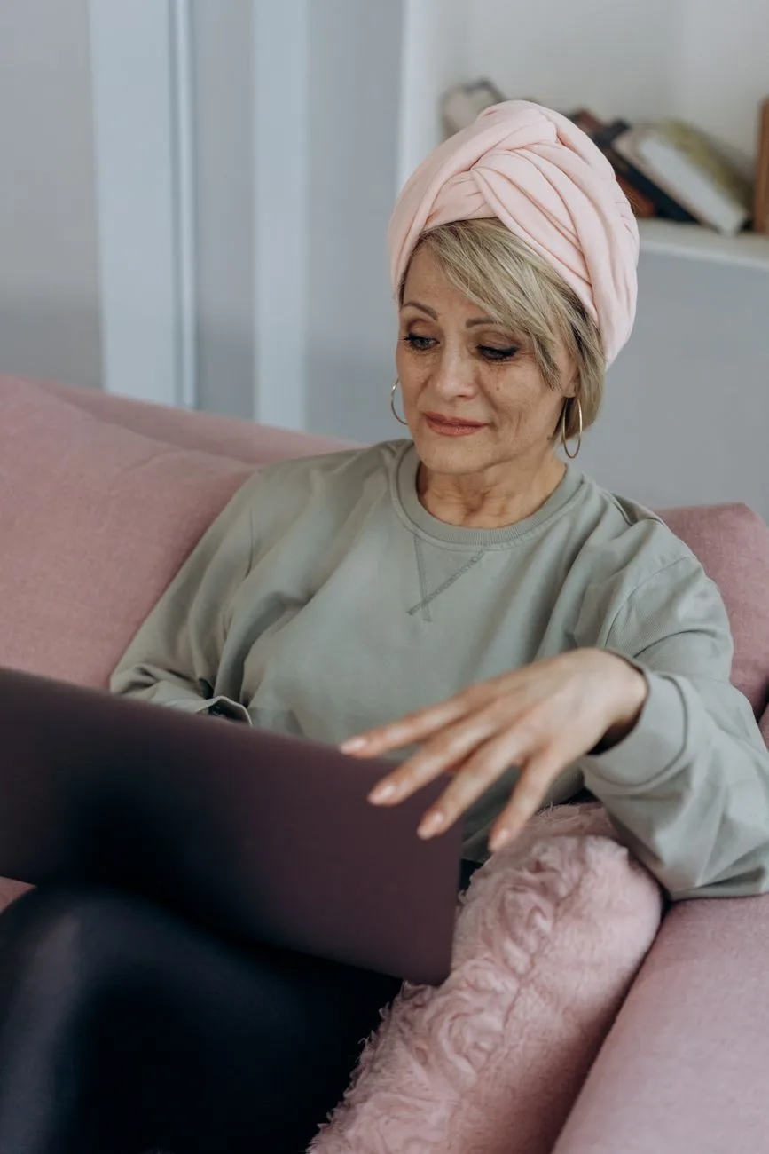 Senior woman with headwrap sitting on a couch using a laptop, demonstrating comfort with technology.