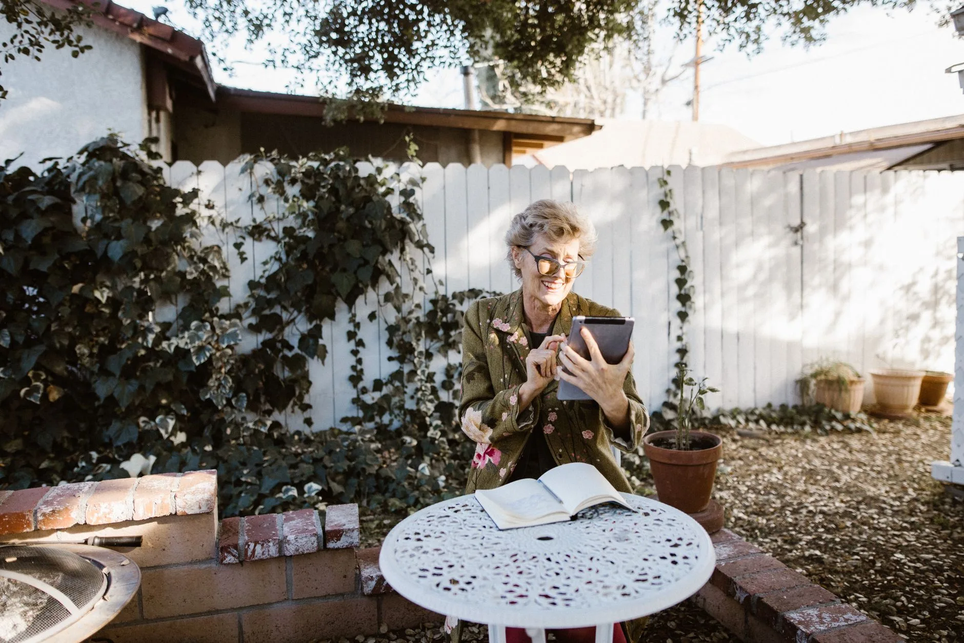 Senior woman enjoying tablet in outdoor garden setting, smiling and relaxed.